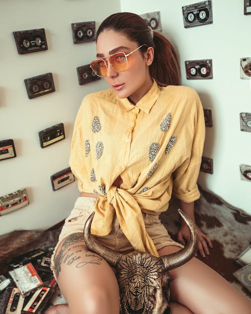 Woman Sitting down  wearing  Sunglasses and Yellow Front-tie Button-up Shirt 