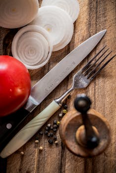 Sliced onions and tomato with cutlery on wooden board, perfect for culinary art concepts.