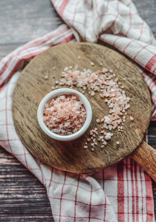 Small white bowl of coarse pink salt on round wooden board