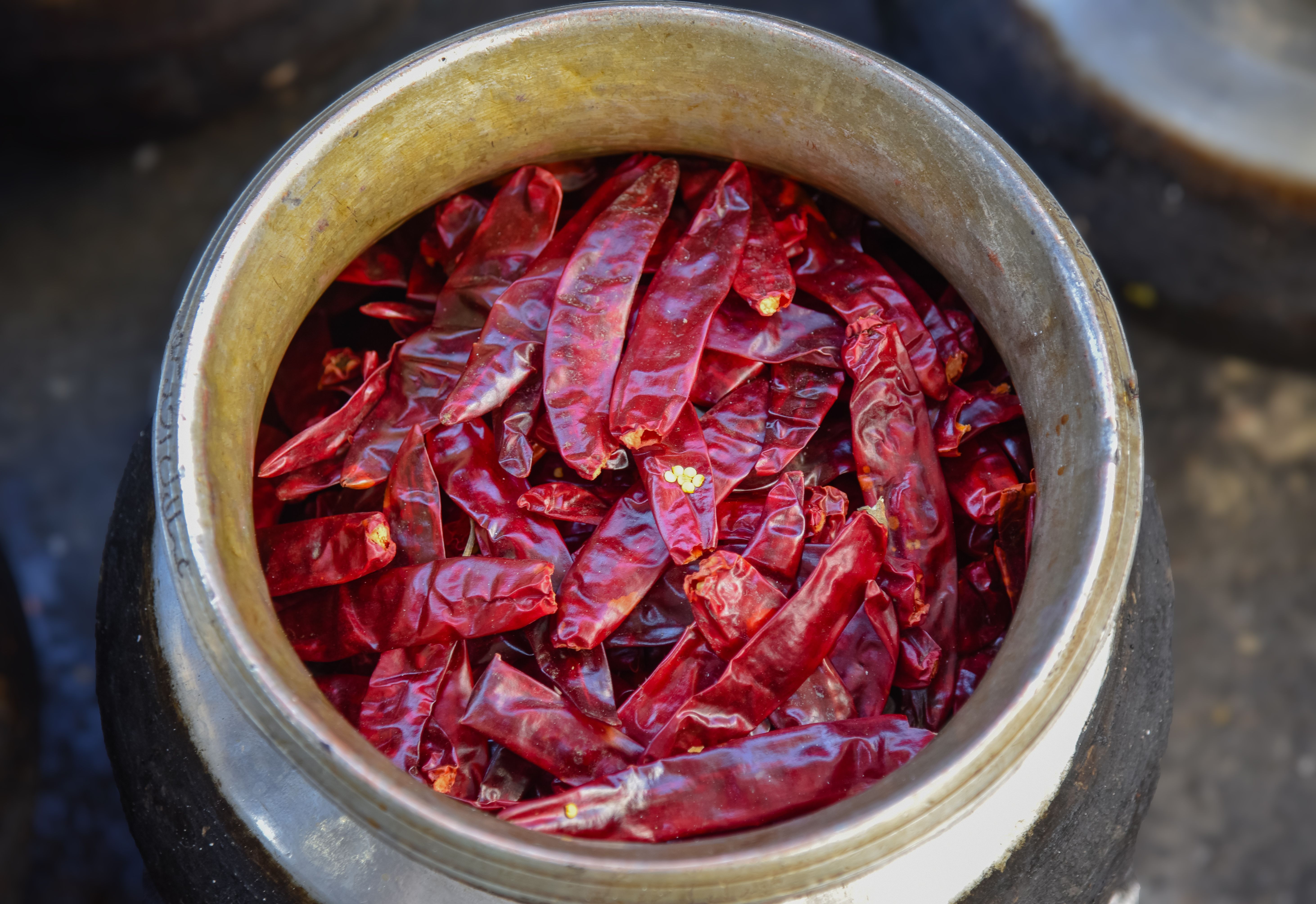 A top-down image of vibrant dry red chilies in a metal bowl, showcasing their texture.