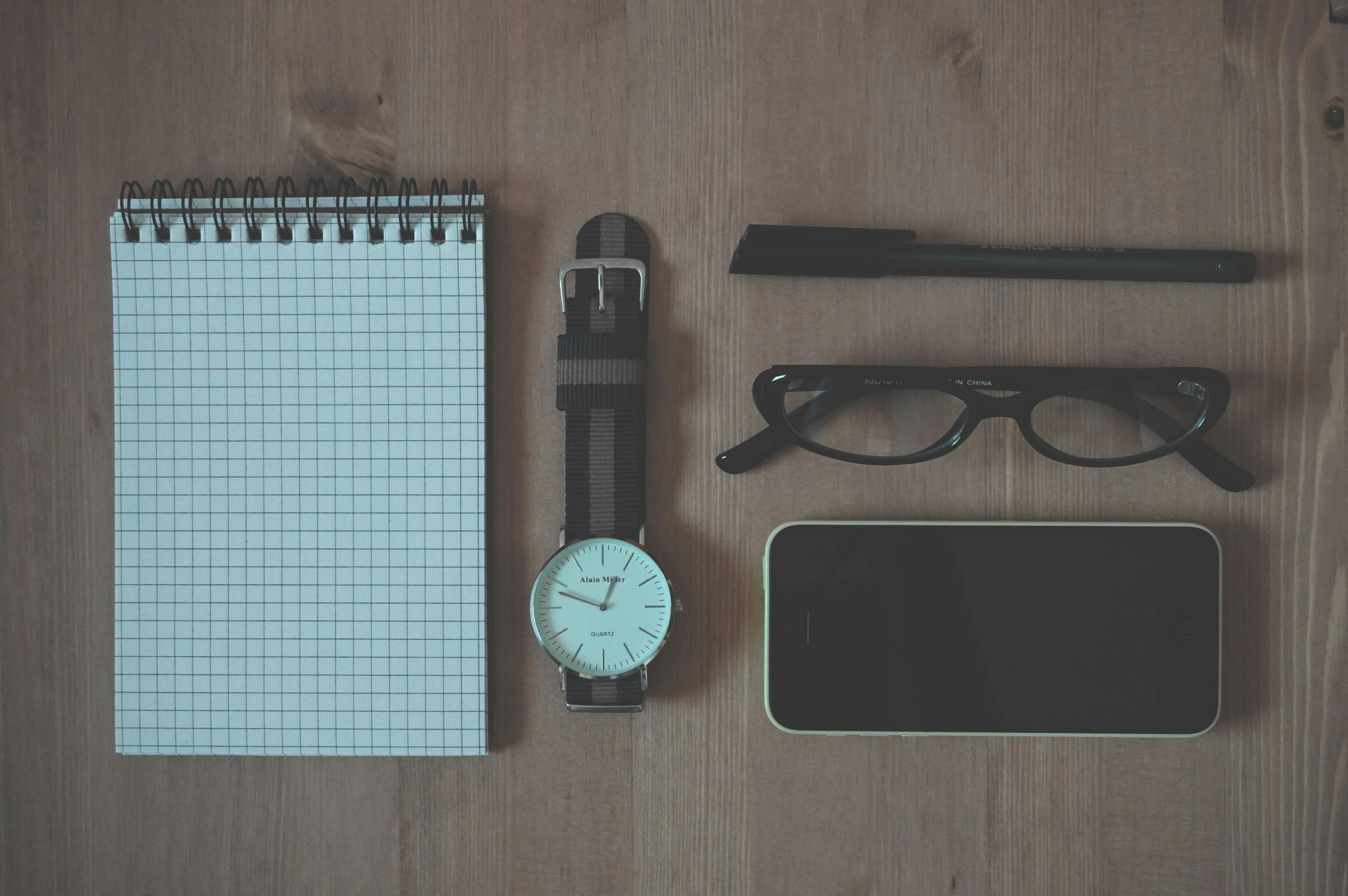 Flat Lay Photography of Graphing Notebook, Watch, Smartphone, Pen, and Eyeglasses