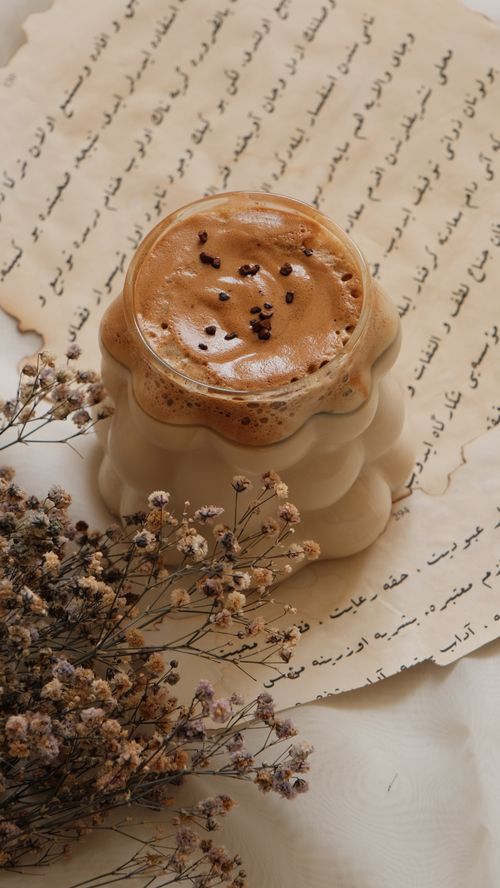 Free Aesthetic dalgona coffee placed on Arabic script paper with dried flowers. Stock Photo