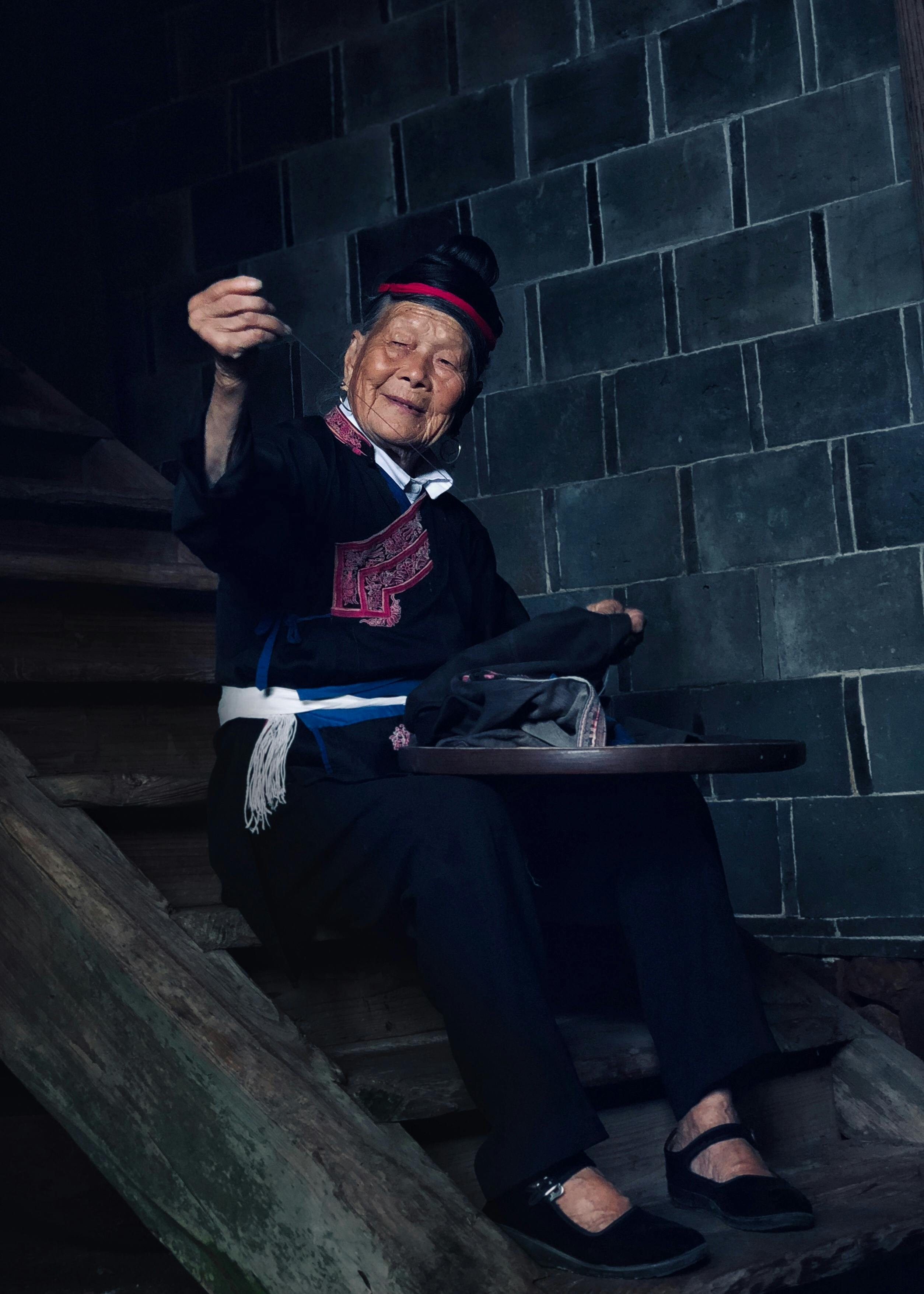 一位快乐的老妇人穿着传统服装，坐在木楼梯上的肖像，中国