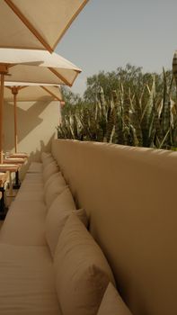 Cozy outdoor patio area with long sofa, cushions, and sunshades, perfect for relaxation.