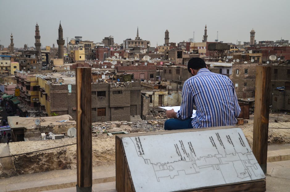 A man observes the urban cityscape of Cairo, featuring minarets and rooftop satellite dishes.