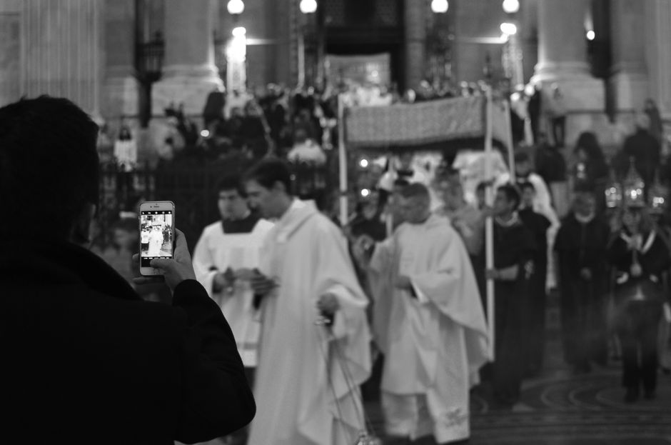 Black and white image of a religious ceremony with priests and a photographer capturing the moment.
