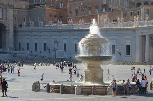 A fountain in the middle of a plaza with people around it