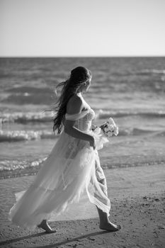 A bride in a flowing dress walks by the sea, capturing a serene wedding moment.