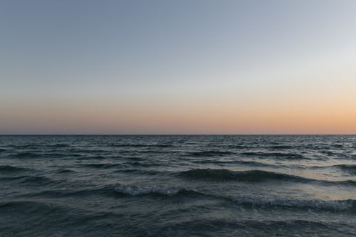 Free Tranquil ocean scene with gentle waves under a clear sky at sunset. Stock Photo
