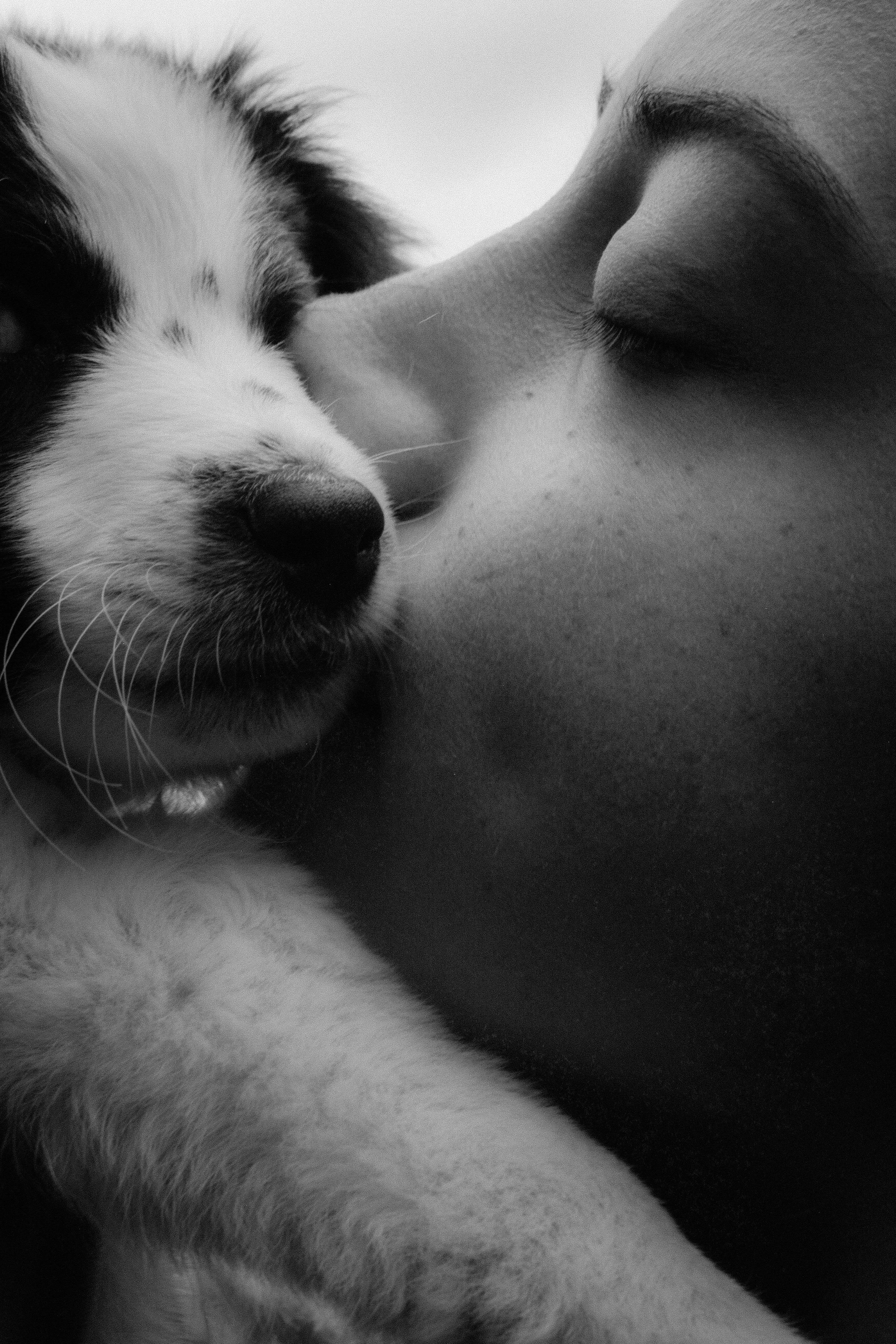 a black and white photo of a woman kissing a dog