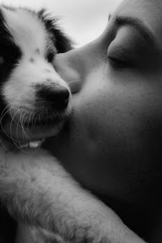 Close-up black and white photo of a woman affectionately kissing a puppy.