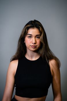 Studio portrait of a young woman wearing a black crop top against a gray background.