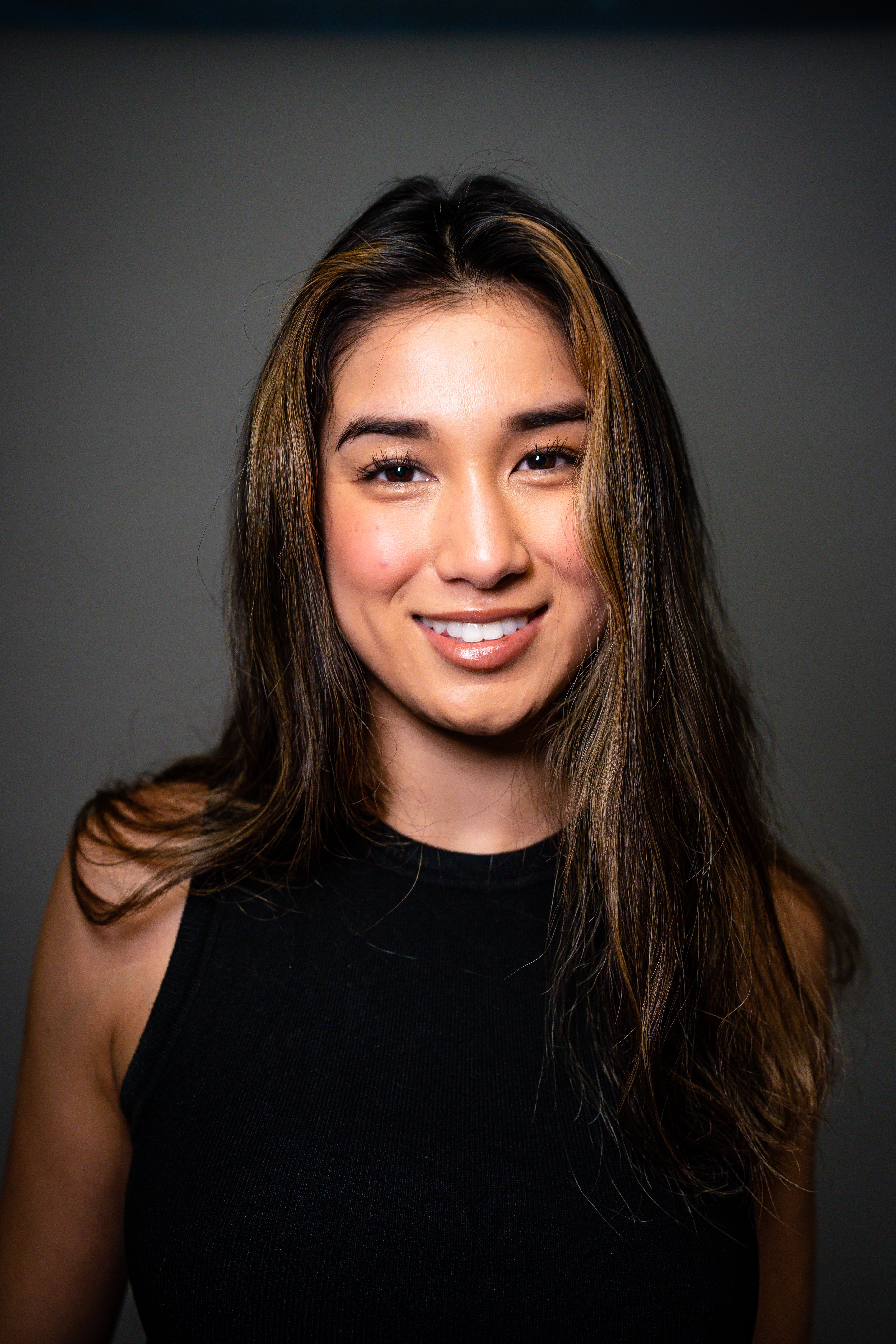 Studio portrait of a young woman with long hair in a black top smiling confidently.