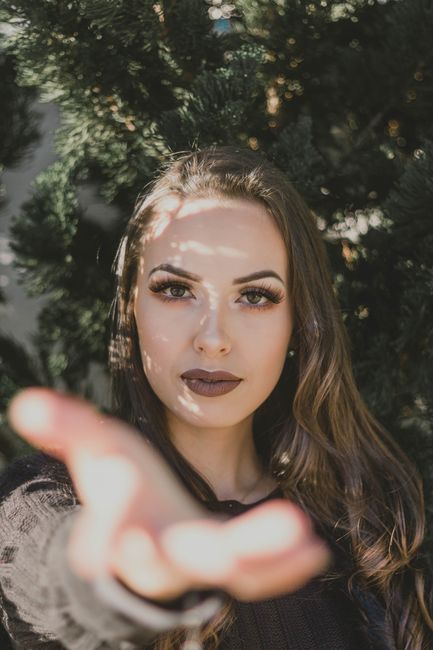 Close-up portrait of a woman reaching forward, surrounded by lush greenery.