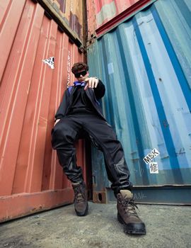 Model posing in trendy urban fashion set against colorful shipping containers.