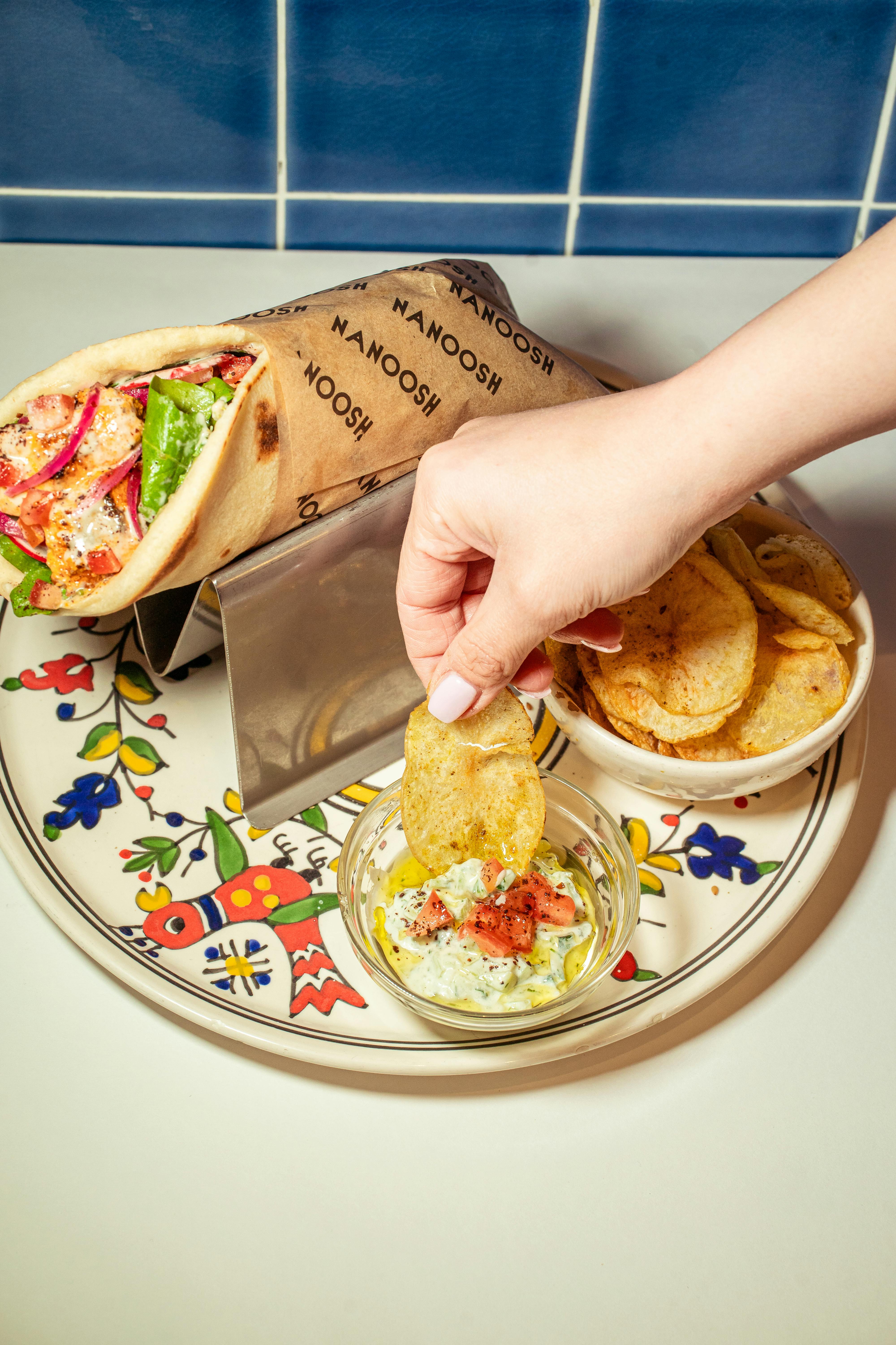 Close-up of a falafel wrap with potato chips and dipping sauce on a decorative plate.