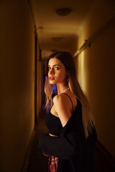 A captivating portrait of a woman with blonde hair standing in a shadowy corridor, evoking mystery.