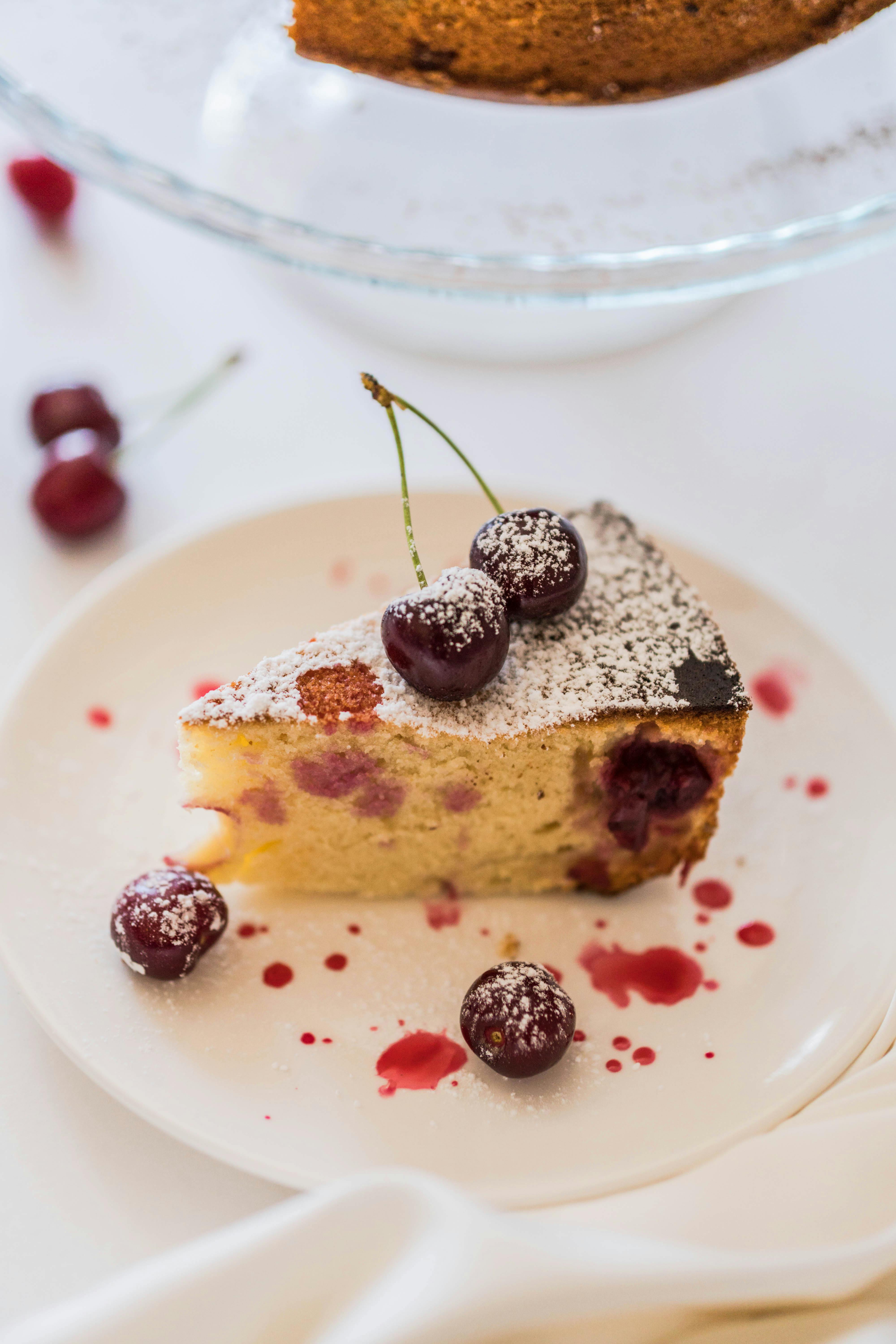 Slice of cherry yogurt cake on a plate with powdered sugar and cherry drizzle, perfect for summer.