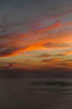 Majestic orange and yellow hues illuminate the sky, creating a stunning sunset scenery above the clouds.