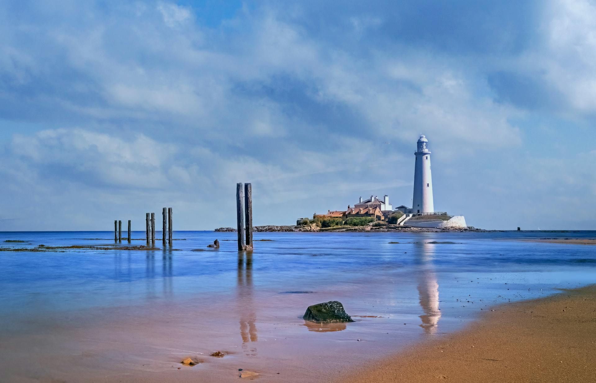 A beautiful lighthouse standing on a small island by the seashore, reflecting on calm waters.
