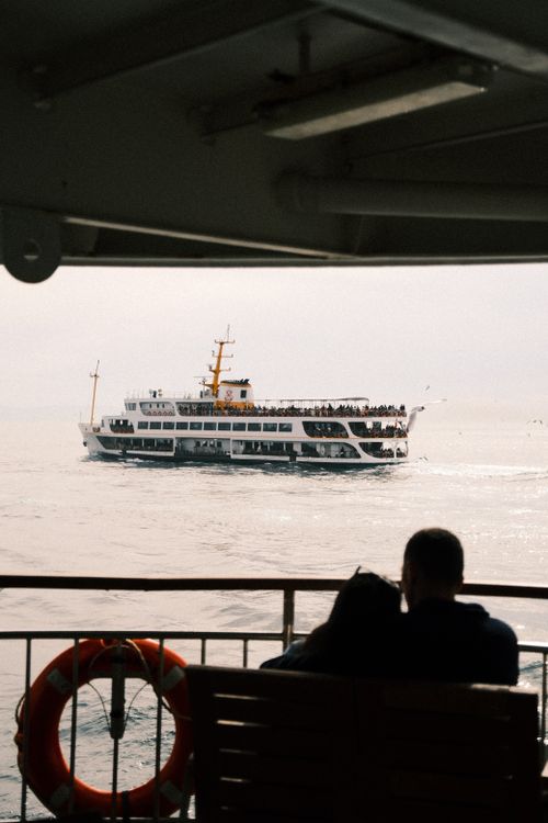 Free People watching a ferry boat sail on the calm sea under a cloudy sky. Stock Photo