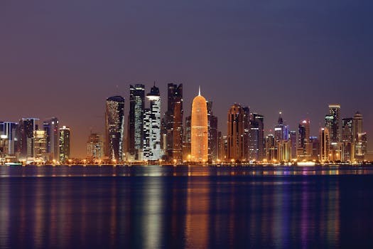 Vibrant night skyline of Doha, Qatar reflecting on the water, showcasing illuminated skyscrapers.