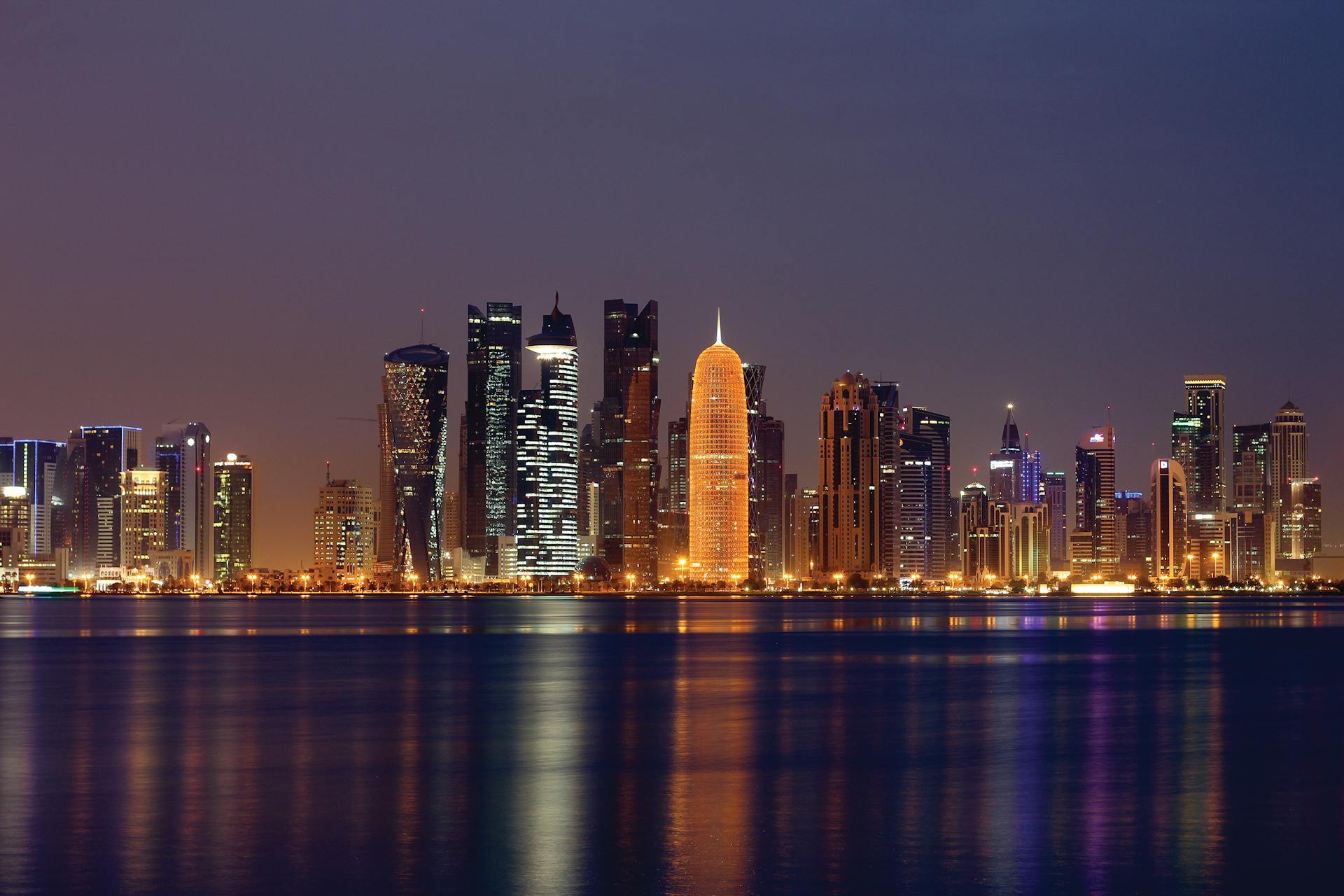 Vibrant night skyline of Doha, Qatar reflecting on the water, showcasing illuminated skyscrapers.