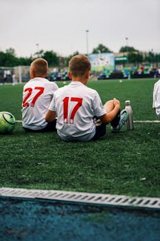 Boys in soccer jerseys sitting on a turf field during a summer game.
