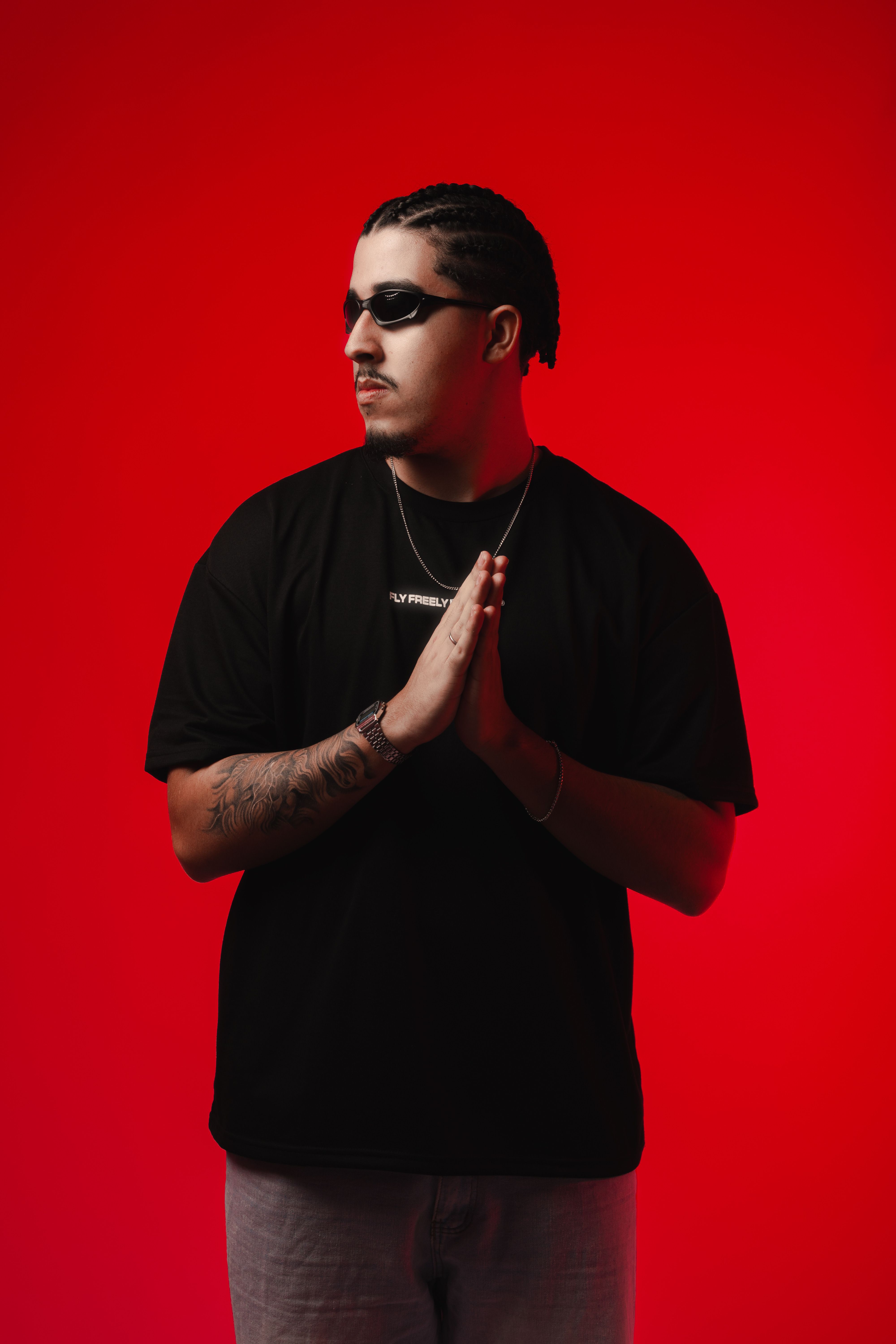 Stylish man in black t-shirt and sunglasses against red backdrop. Studio shoot.