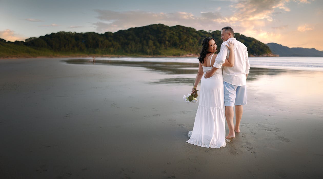 A bride and groom standing on the beach at sunset