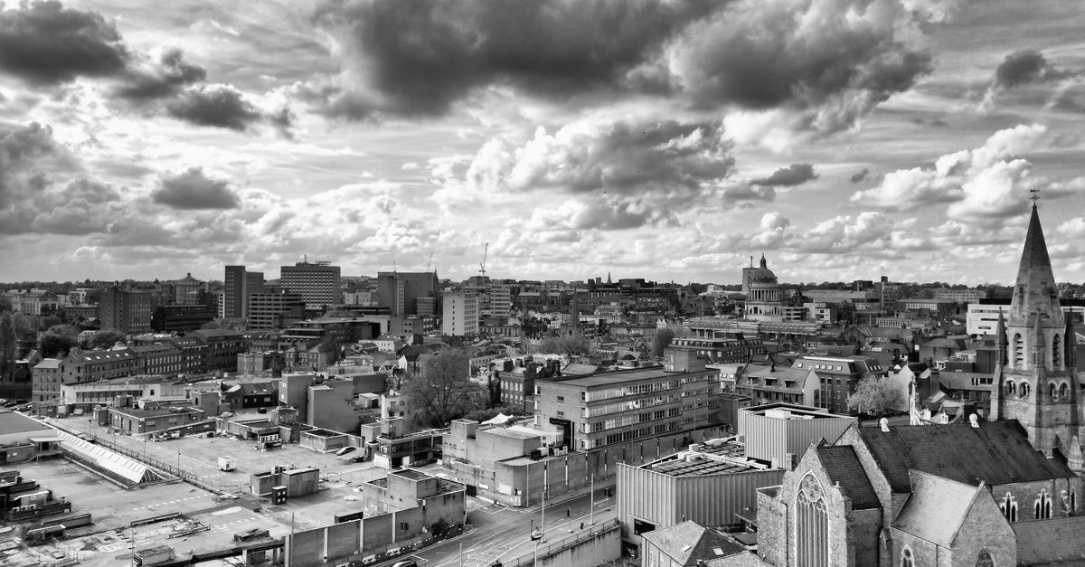 Black and white aerial view of Nottingham cityscape with rooftops, canal and dramatic clouds overhead