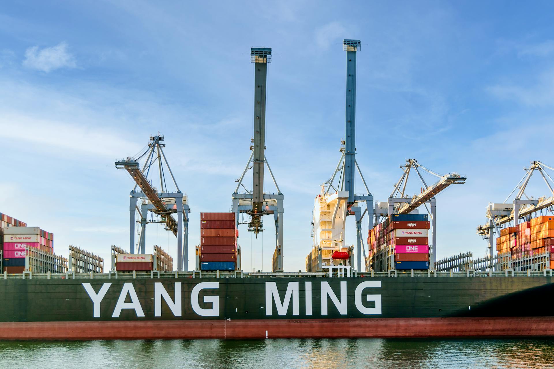 Large container ship at port with cranes loading cargo in a busy harbor.