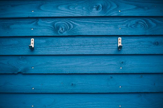 A vibrant blue wooden wall with two metal hooks creates a striking visual pattern.