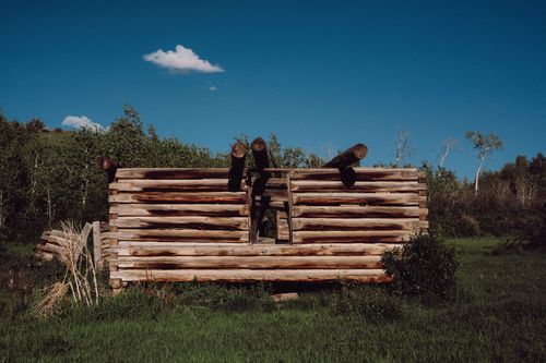 Free An abandoned wooden cabin sits in a lush green meadow under a clear blue sky. Stock Photo