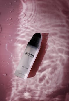 Sophisticated skincare product bottle with water reflections on a pink textured surface. Ideal for beauty ads.