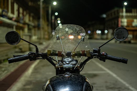 A vintage motorcycle with rain-speckled windshield on empty city streets of Paro, Bhutan at night.