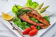 白色盘子上摆放着美味的烤三文鱼排，搭配鳄梨、生菜、樱桃番茄和柠檬片