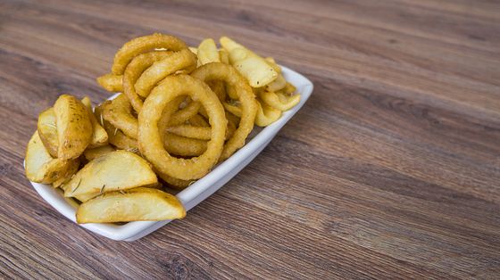 White rectangular dish piled with crispy onion rings and seasoned potato wedges on wood