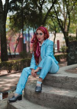 Stylish redhead woman in a blue suit and headscarf sitting on stone steps in a park.