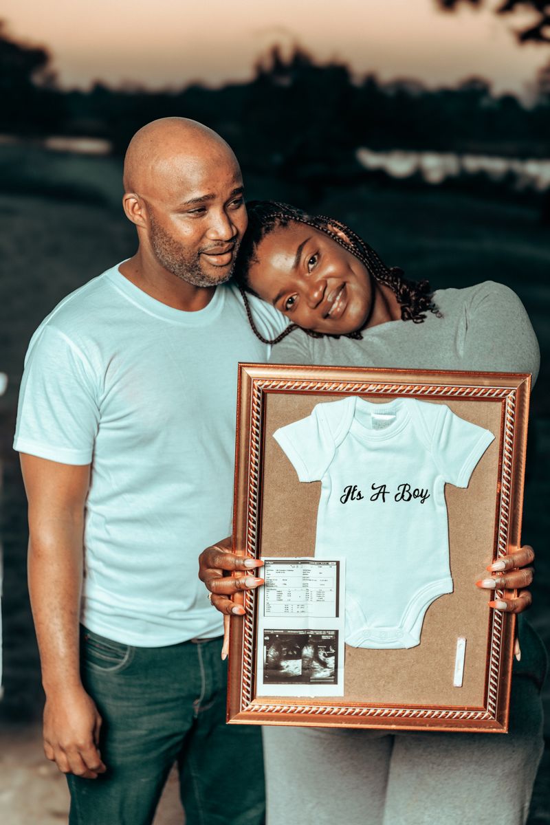 Joyful couple holding baby announcement frame during sunset outdoors.