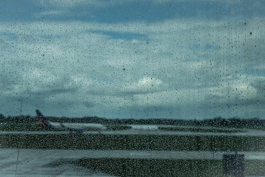 Airplane in the distance through raindrop-covered window at airport.