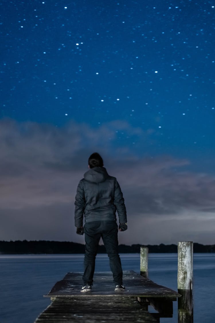 A Man In Black Jacket Standing On Wooden Dock