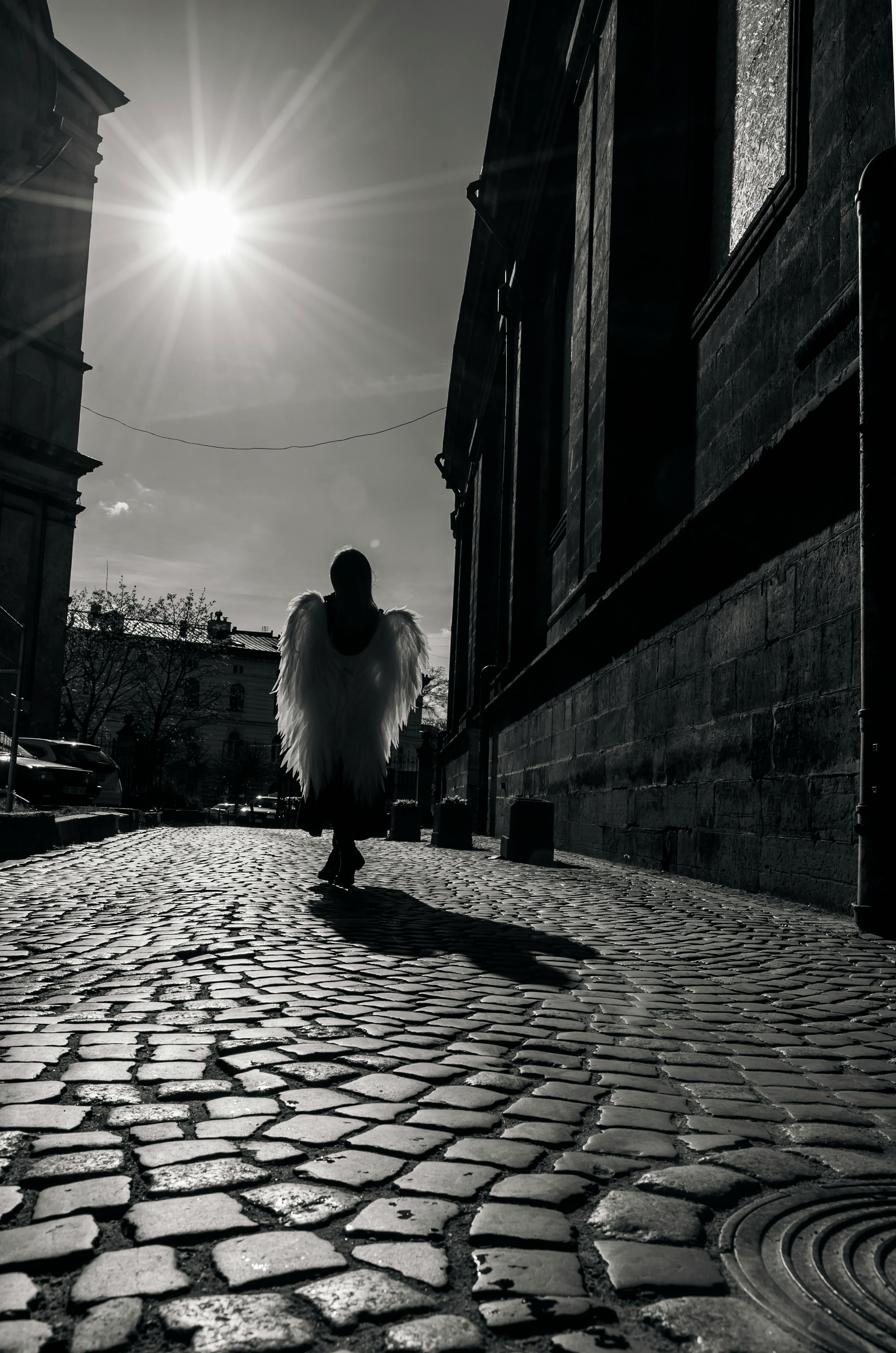 Black and white photo of a silhouetted figure with angel wings on a cobblestone street in Lviv, Ukraine.