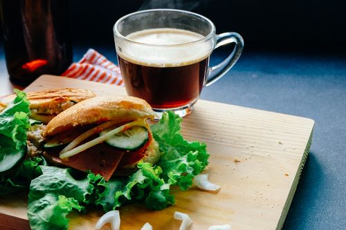 Free Tasty sandwich with fresh ingredients next to a steaming cup of coffee on a wooden board. Stock Photo