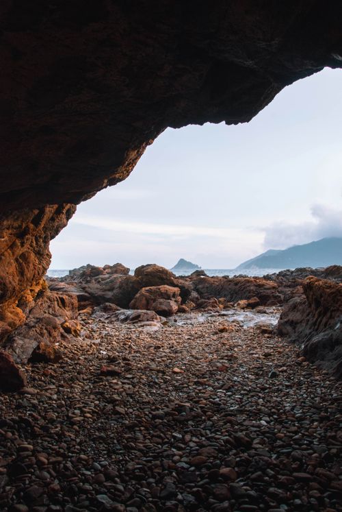 Free A picturesque view from within a seaside cave overlooking rocky formations and distant mountains. Stock Photo