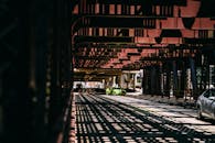 汽车行驶在钢桥下，在道路上投下戏剧性的阴影图案