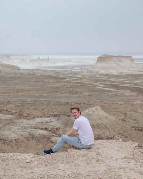 Free A man in a white shirt and jeans sitting on the vast Ustyurt Plateau, Kazakhstan, surrounded by stunning desolate landscapes. Stock Photo
