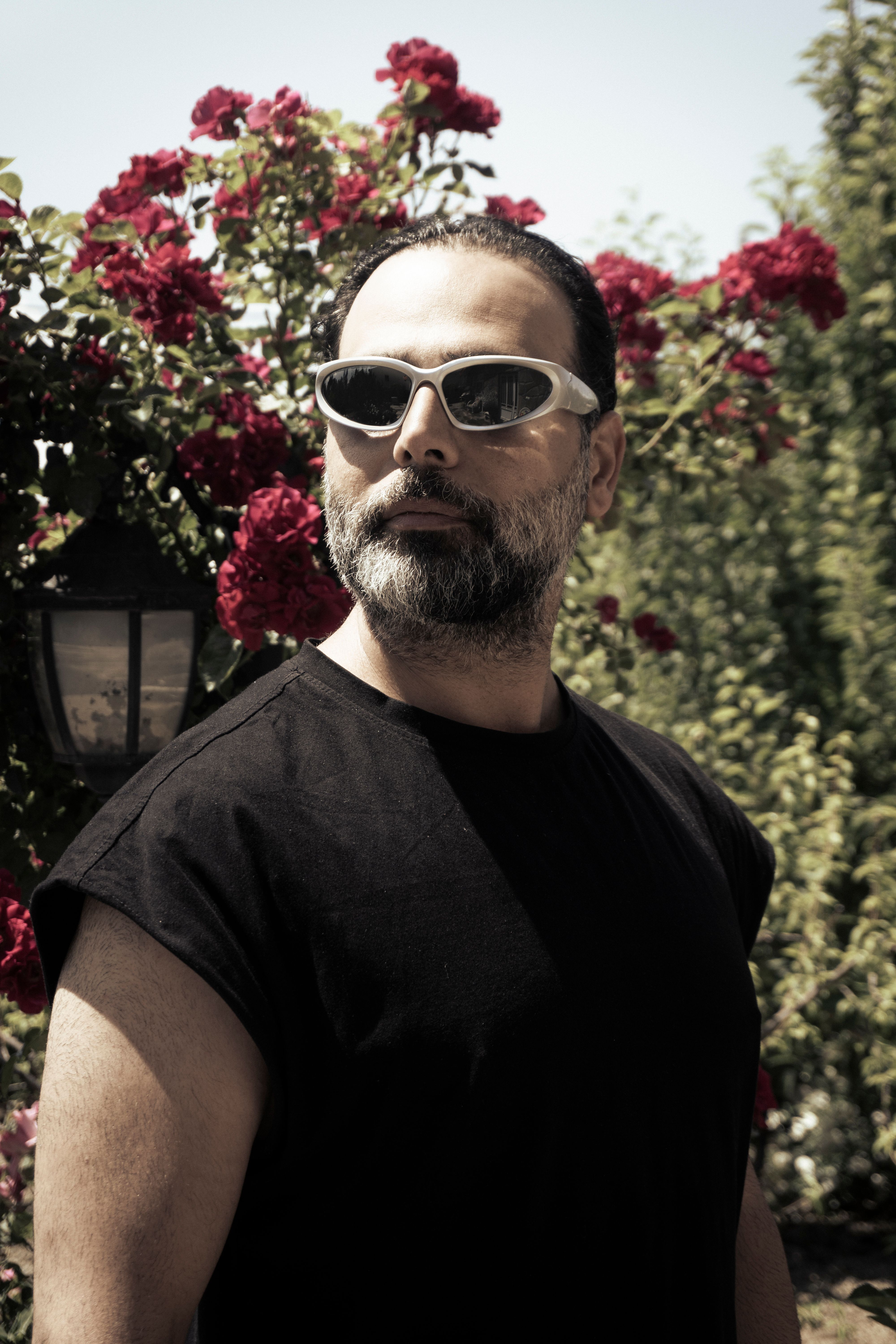 Fashionable man wearing sunglasses and a t-shirt in a garden with blooming red roses.