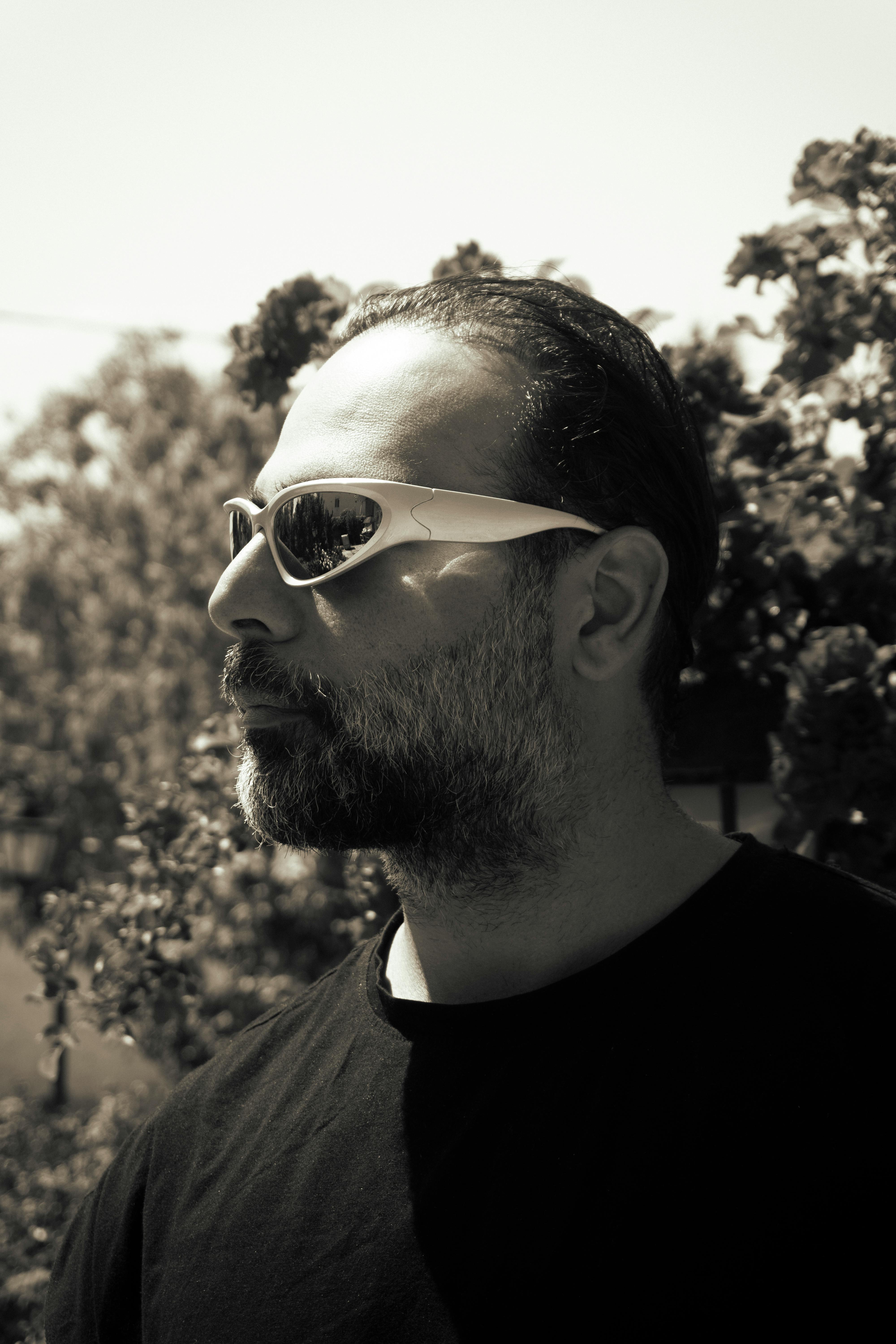 Profile portrait of bearded man wearing sunglasses against a garden backdrop in Hamedan, Iran.