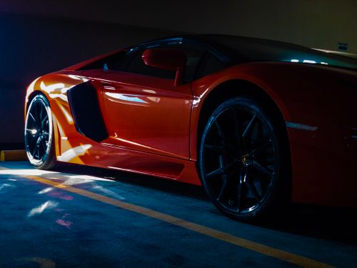 Free Close-up of a vibrant orange sports car parked in a sunlit garage, showcasing luxury and modern design. Stock Photo